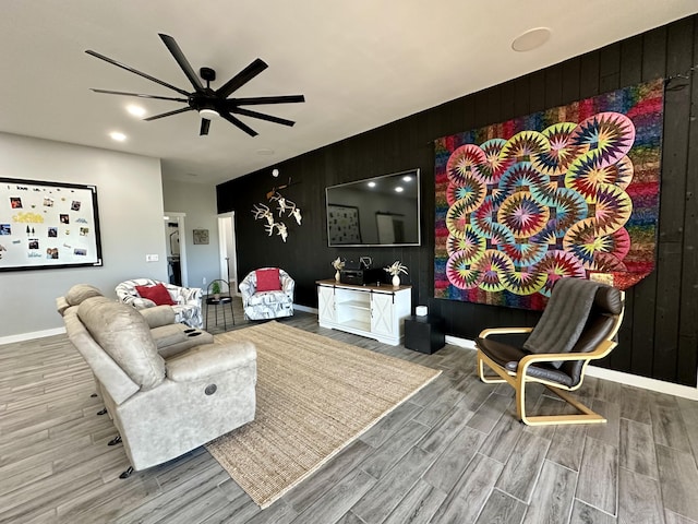living area featuring baseboards, wood walls, wood finished floors, and ceiling fan