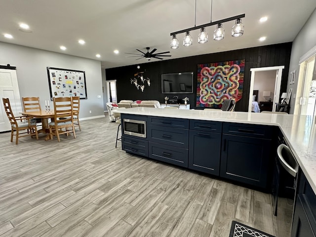 kitchen with a barn door, stainless steel appliances, light wood-style floors, light countertops, and a ceiling fan