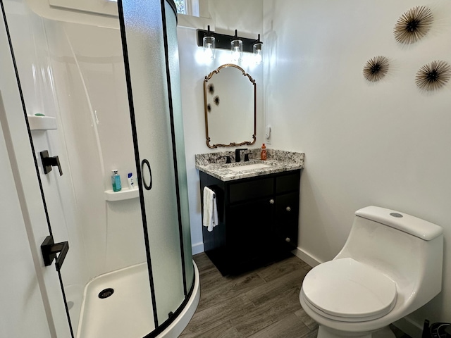 bathroom with a shower stall, baseboards, toilet, wood finished floors, and vanity