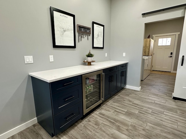 bar featuring baseboards, beverage cooler, light wood-type flooring, and washing machine and clothes dryer