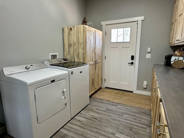 clothes washing area with baseboards, cabinet space, washer and clothes dryer, and light wood-style flooring
