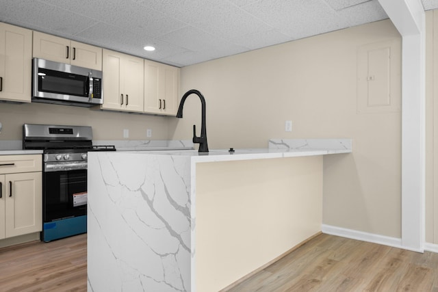 12320 E Houghton Lake Dr, Houghton Lake, MI 48629 - kitchen featuring appliances with stainless steel finishes, light wood-type flooring, a peninsula, a paneled ceiling, and light stone countertops