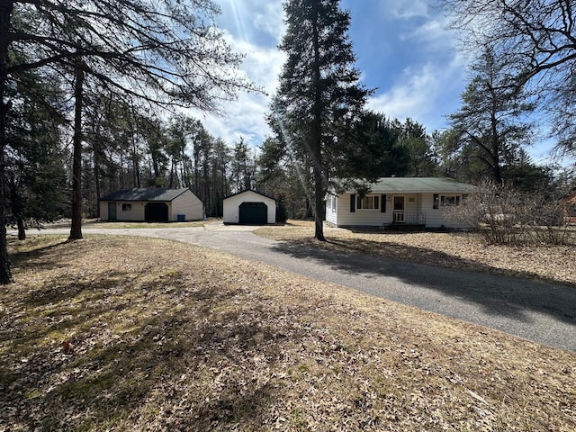 exterior space with a porch, aphalt driveway, a detached garage, and an outdoor structure