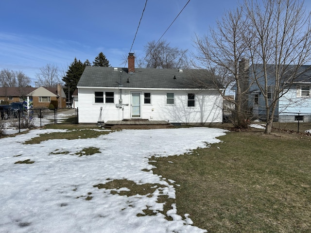 snow covered house with a chimney, fence, and a lawn