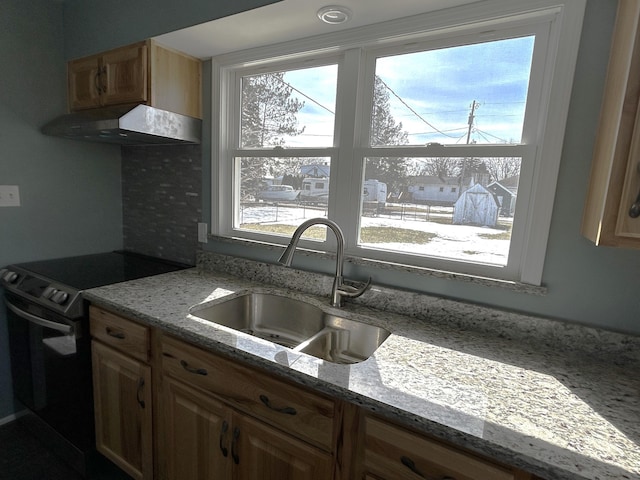 kitchen with electric range, under cabinet range hood, a sink, and light stone countertops