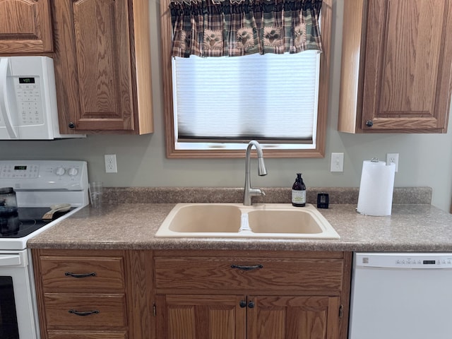 kitchen with a sink, brown cabinets, dark countertops, and white appliances