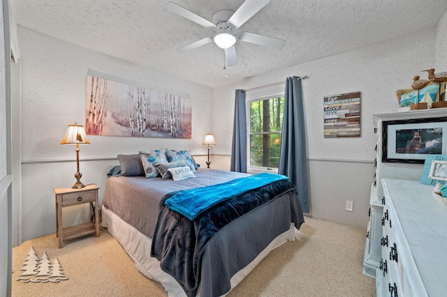 bedroom featuring a ceiling fan, a textured ceiling, light carpet, and wainscoting