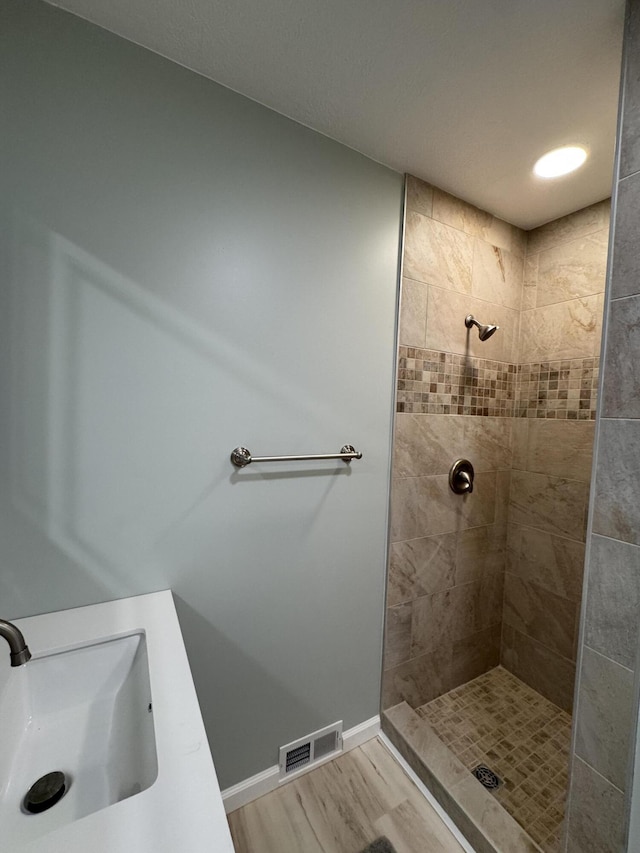 bathroom featuring tiled shower, visible vents, baseboards, and a sink