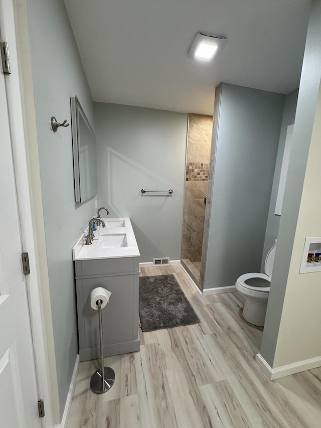 bathroom featuring vanity, toilet, wood finished floors, walk in shower, and baseboards
