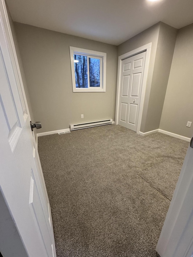 unfurnished bedroom with carpet, baseboard heating, and baseboards