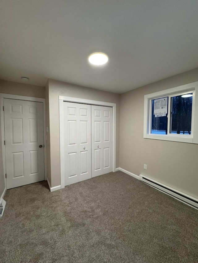 unfurnished bedroom featuring baseboard heating, a closet, baseboards, and carpet floors