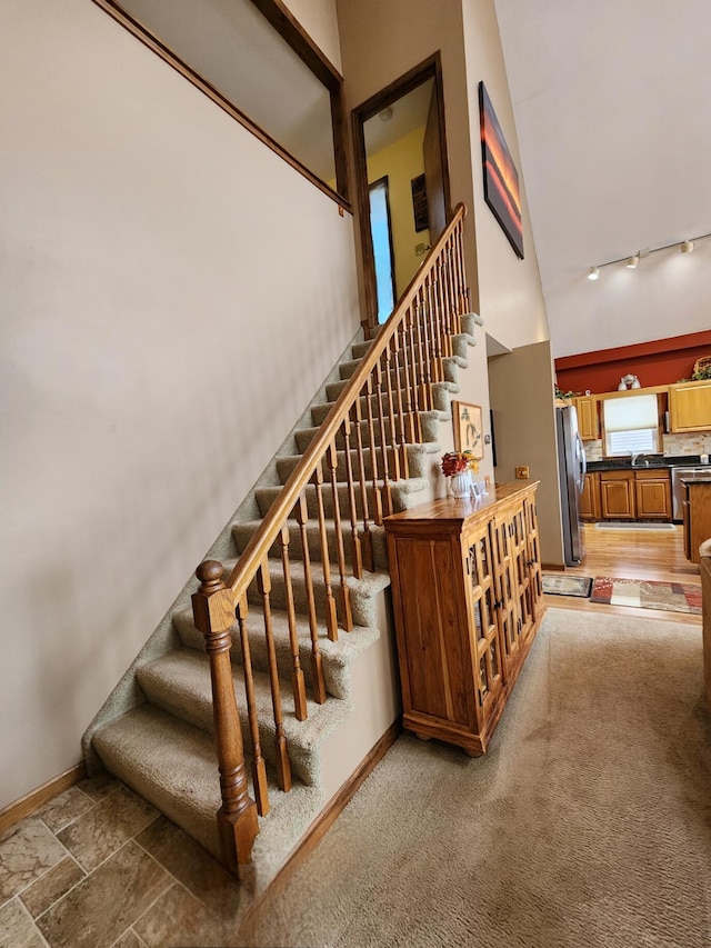 stairs featuring a high ceiling, baseboards, and rail lighting