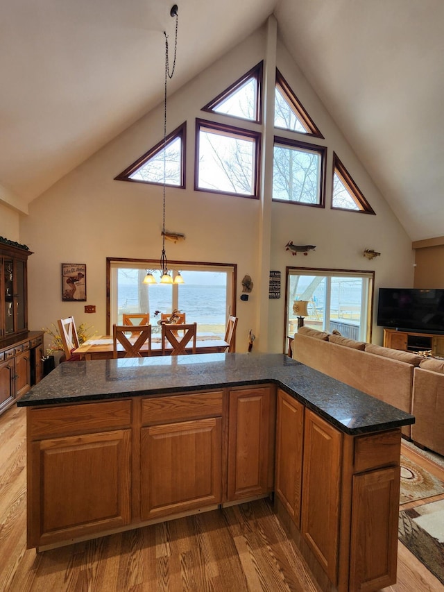 kitchen with dark stone counters, light wood-type flooring, brown cabinets, and high vaulted ceiling