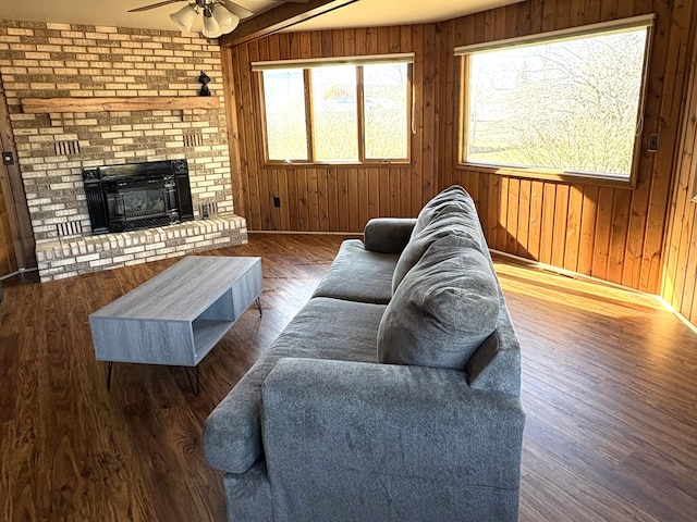 living area with wood walls, a brick fireplace, wood finished floors, baseboards, and ceiling fan