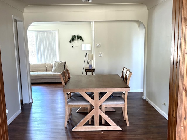 dining room featuring arched walkways, baseboards, and dark wood finished floors
