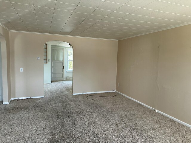 unfurnished room featuring carpet floors, baseboards, arched walkways, and ornamental molding
