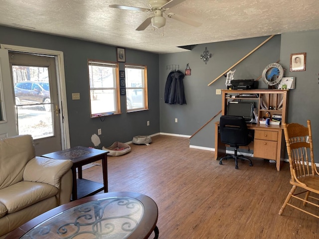 living area featuring ceiling fan, baseboards, wood finished floors, and a textured ceiling