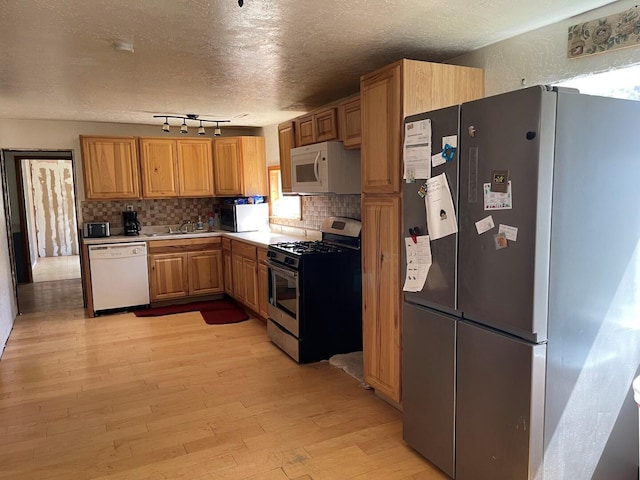 kitchen with backsplash, stainless steel appliances, a textured ceiling, and light wood-style flooring