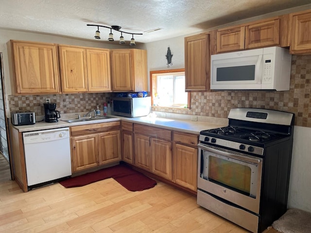 kitchen featuring light wood-style flooring, a sink, backsplash, light countertops, and appliances with stainless steel finishes