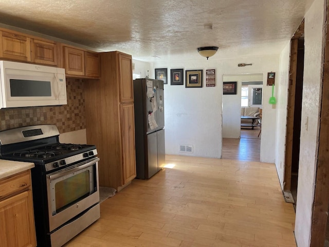 kitchen with stainless steel range with gas cooktop, white microwave, light wood-style flooring, visible vents, and freestanding refrigerator
