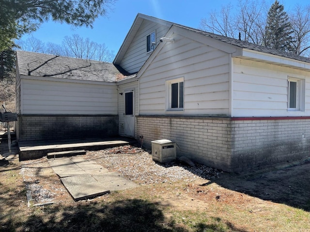 exterior space with brick siding and roof with shingles