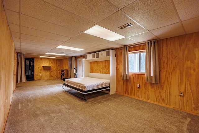carpeted bedroom with wood walls, a drop ceiling, and visible vents