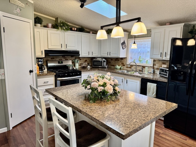 10525 Alpenhof Dr, Grayling, MI 49738 - kitchen with black appliances, a sink, a textured ceiling, range hood, and a breakfast bar area