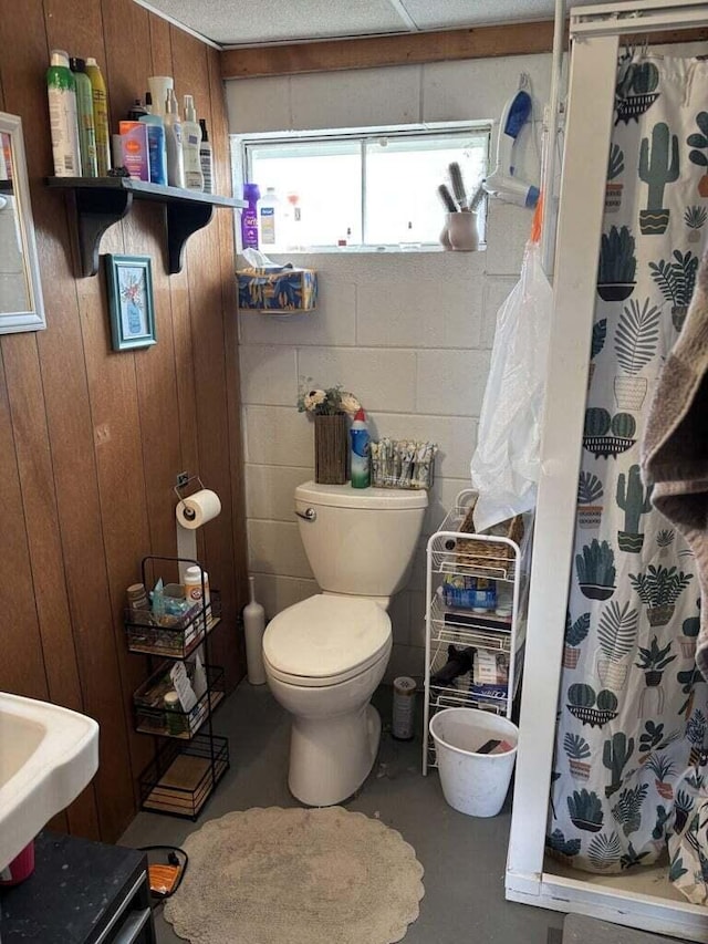 bathroom with a shower stall, a sink, concrete flooring, wooden walls, and toilet