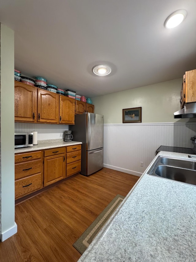 kitchen with wainscoting, under cabinet range hood, a sink, dark wood finished floors, and stainless steel appliances