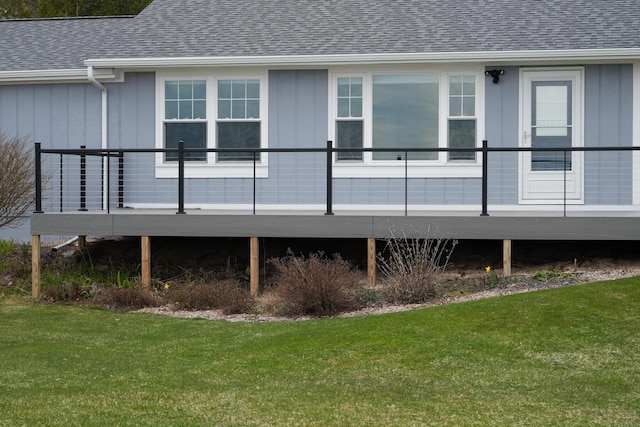 back of property featuring roof with shingles, board and batten siding, a yard, and a deck