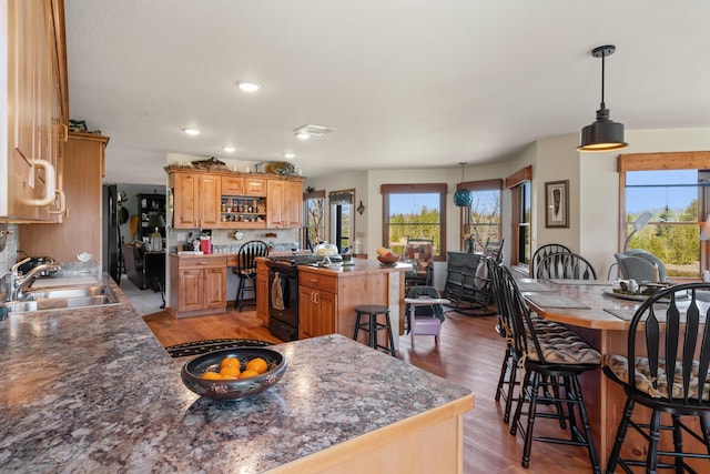 kitchen with light wood-style floors, black gas range, a kitchen bar, and a sink