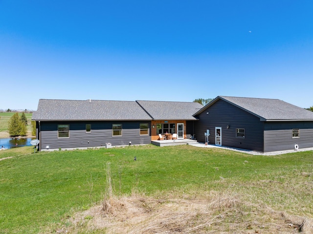 rear view of property with a yard, a patio area, and roof with shingles