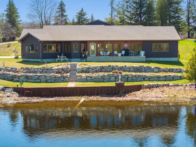 rear view of property with a water view, a yard, and a shingled roof