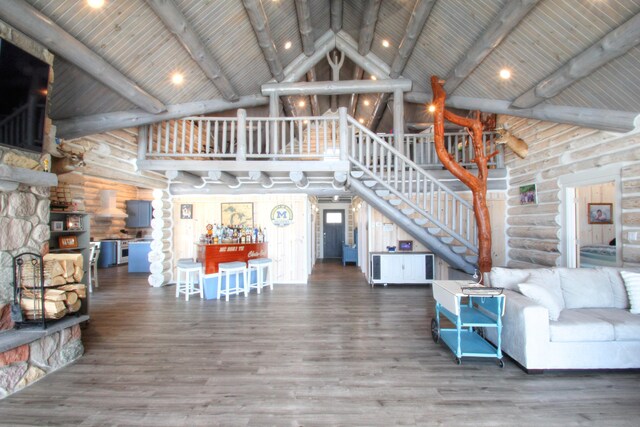 living area featuring beamed ceiling, rustic walls, high vaulted ceiling, stairs, and wood finished floors