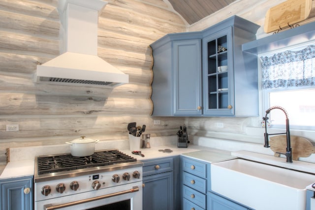kitchen with glass insert cabinets, a sink, blue cabinets, exhaust hood, and gas stove