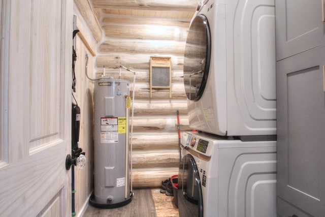 clothes washing area featuring rustic walls, stacked washer and clothes dryer, laundry area, wood finished floors, and electric water heater