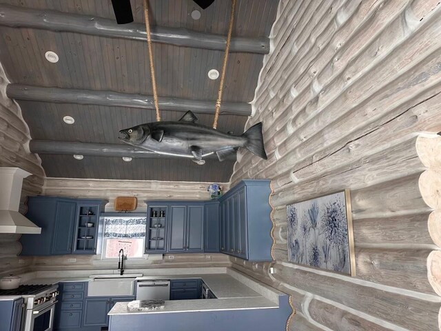 kitchen with rustic walls, a sink, stainless steel appliances, blue cabinetry, and a towering ceiling