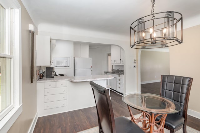 dining space featuring arched walkways, baseboards, a chandelier, and dark wood-type flooring