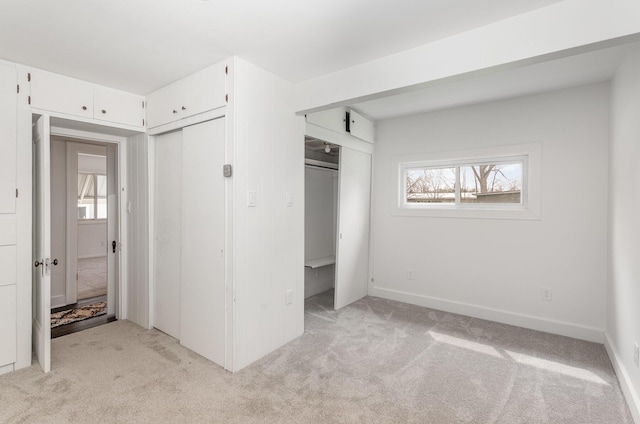 unfurnished bedroom with two closets, light colored carpet, and baseboards