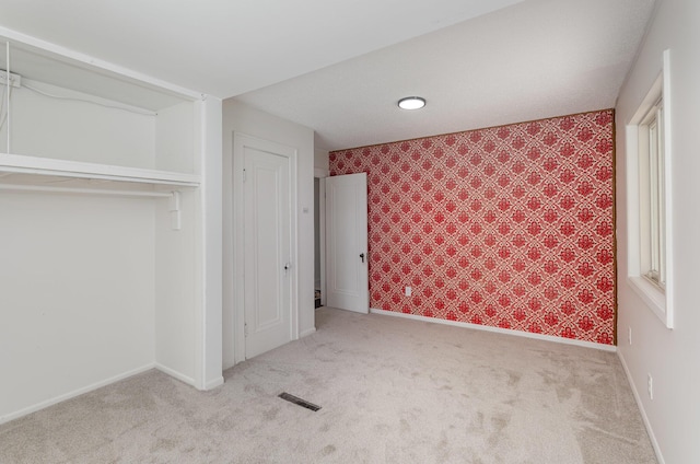 unfurnished bedroom with a closet, visible vents, wallpapered walls, and carpet floors