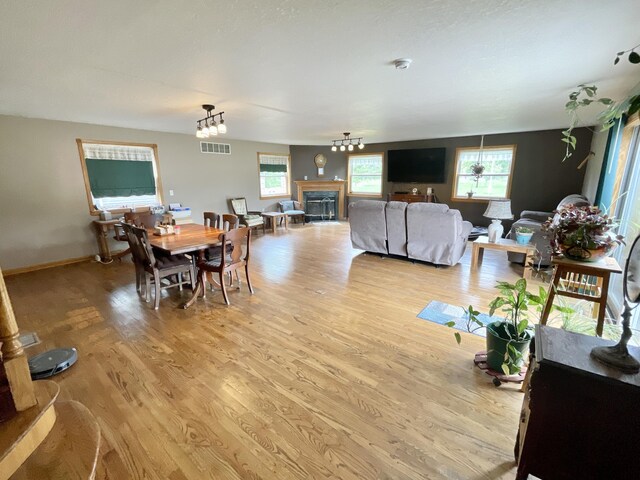 dining space with a glass covered fireplace, baseboards, visible vents, and light wood-style floors
