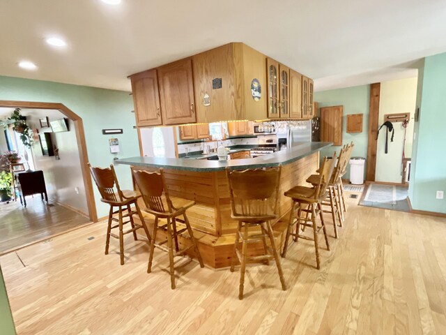 kitchen featuring dark countertops, stainless steel appliances, light wood finished floors, and glass insert cabinets