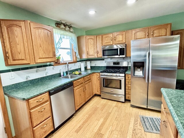 kitchen featuring dark countertops, tasteful backsplash, a sink, light wood finished floors, and appliances with stainless steel finishes