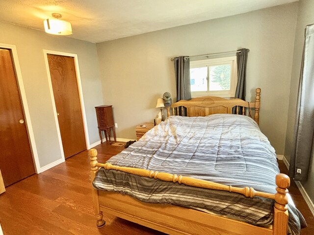 bedroom with two closets, baseboards, and wood finished floors