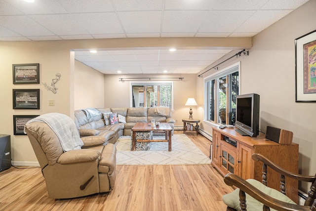 living room featuring baseboard heating, light wood-type flooring, baseboards, a drop ceiling, and recessed lighting