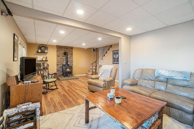 living room featuring a wood stove, light wood-type flooring, stairs, a drop ceiling, and recessed lighting