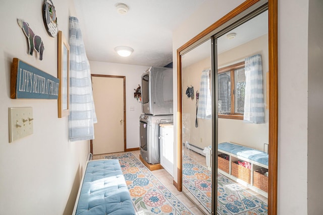hall featuring light tile patterned floors, a baseboard heating unit, and stacked washer / dryer
