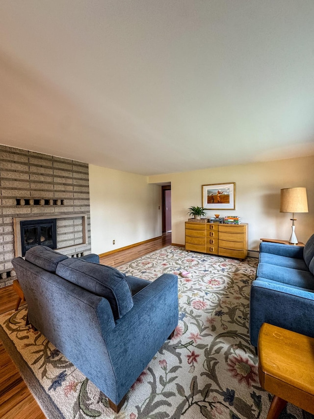 living area featuring baseboards, a brick fireplace, and wood finished floors