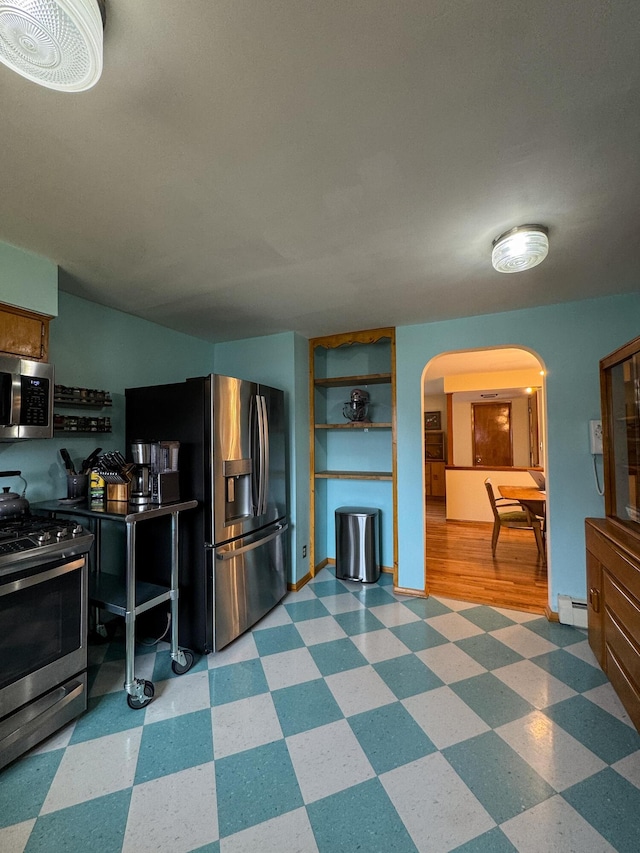 kitchen with arched walkways, a baseboard heating unit, appliances with stainless steel finishes, and tile patterned floors
