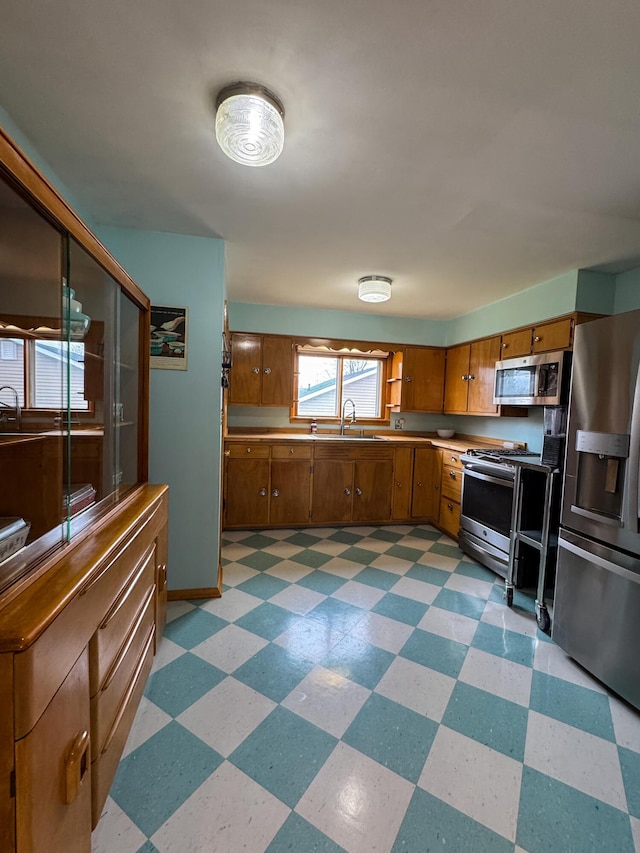 kitchen with brown cabinetry, a sink, light floors, and appliances with stainless steel finishes